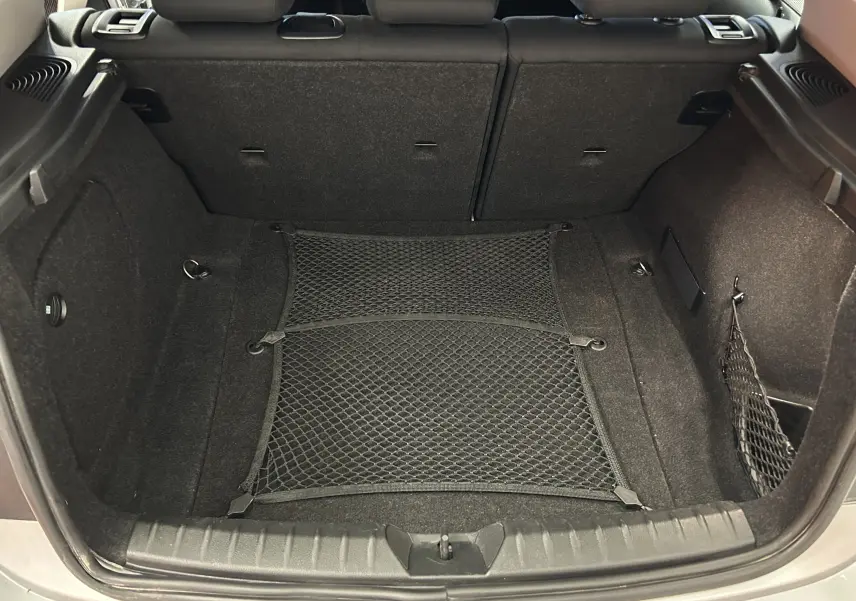 Coffre ouvert de la BMW Série 1 gris 2014, montrant un filet de rangement et banquette arrière rabattue partiellement.