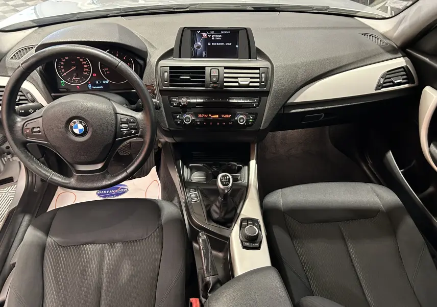 Intérieur BMW Série 1 gris 2014, vue frontale du tableau de bord avec volant, console centrale et sièges tissu noirs.
