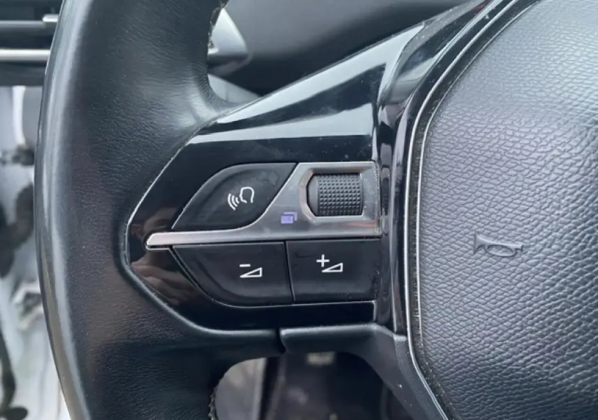 Gros plan sur les commandes gauche du volant noir du Peugeot 3008 blanc, avec boutons de volume et appel mains-libres.