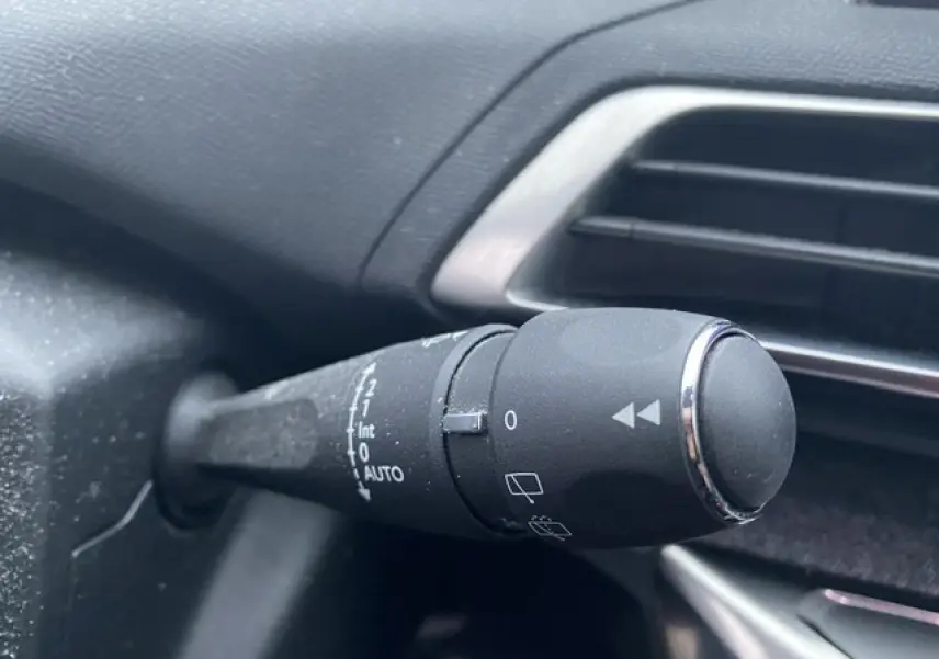 Gros plan sur la commande d’essuie-glace à gauche du volant dans l’habitacle du Peugeot 3008 blanc 2017.