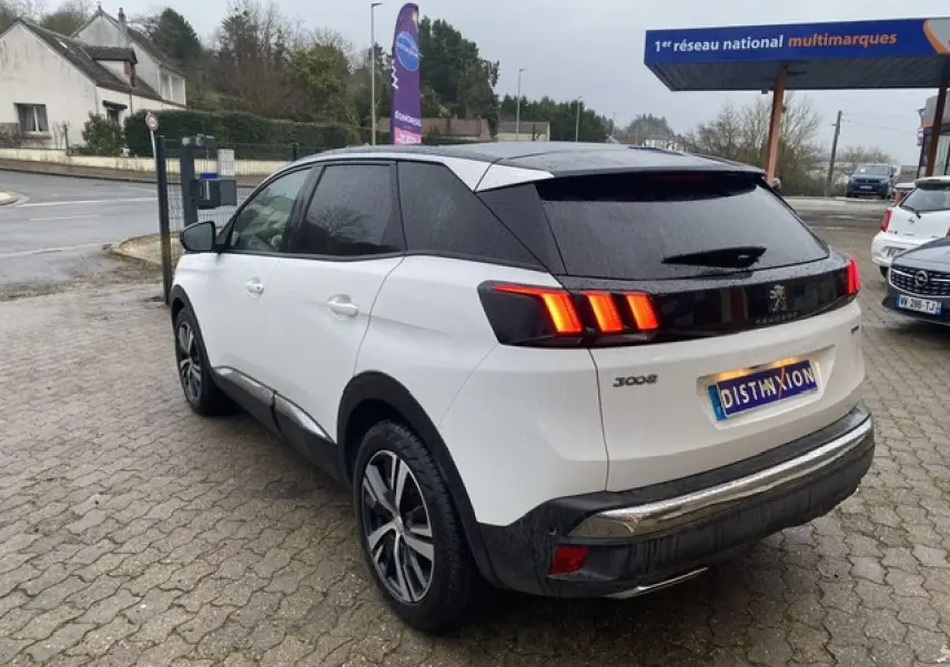 Vue 3/4 arrière droite d'un Peugeot 3008 blanc avec toit noir et feux arrière LED allumés sur parking.