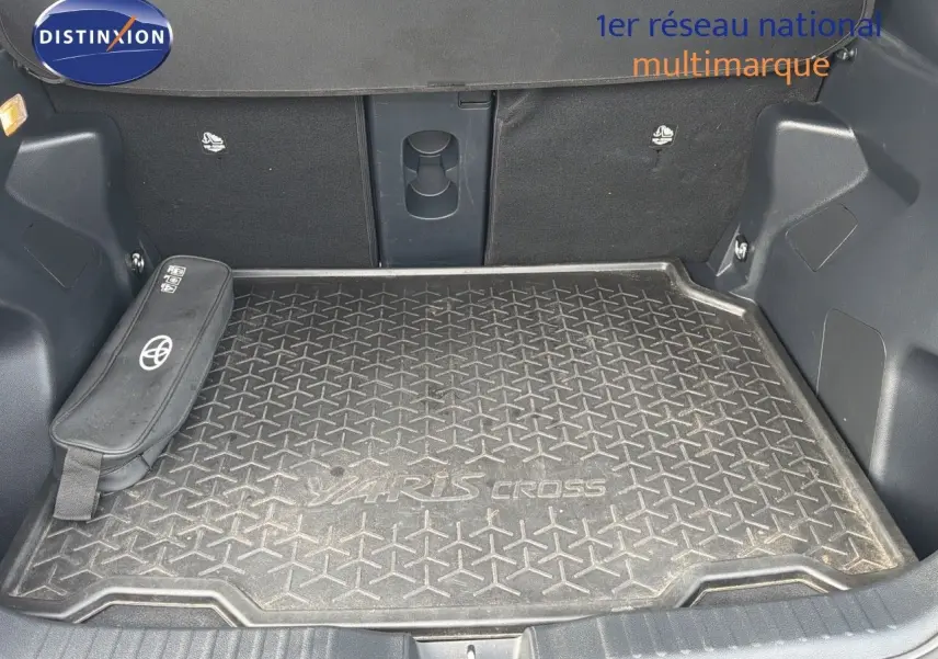 Coffre ouvert d'une Toyota Yaris Cross gris minéral, avec tapis de coffre marqué Yaris Cross et rangement latéral Toyota.