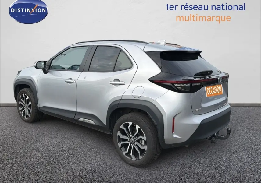Toyota Yaris Cross gris minéral vue 3/4 arrière droit avec jantes bi-ton et attelage visible.