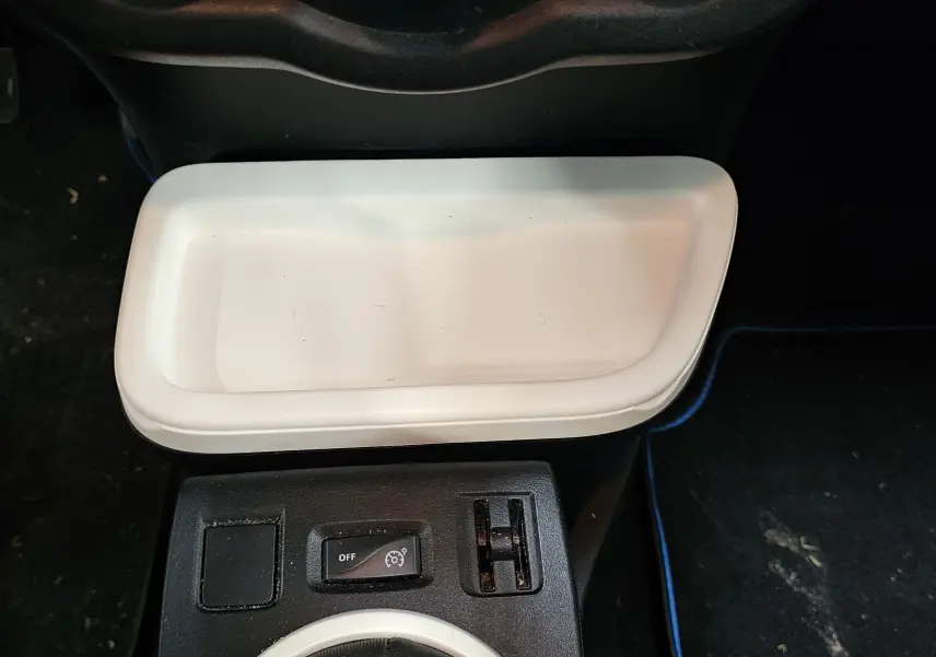 Vue rapprochée de la console centrale d'une Renault Twingo III gris lunaire, avec rangement blanc et commandes de régulateur de vitesse.