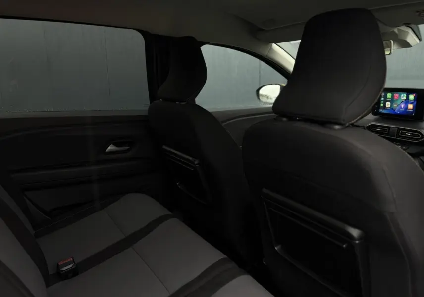 Vue intérieure arrière du Dacia Jogger gris urbain, montrant les sièges et l'écran tactile du tableau de bord.