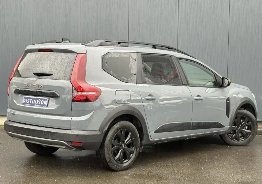 Vue 3/4 arrière droite d'un Dacia Jogger gris urbain avec jantes noires et barres de toit modulaires.