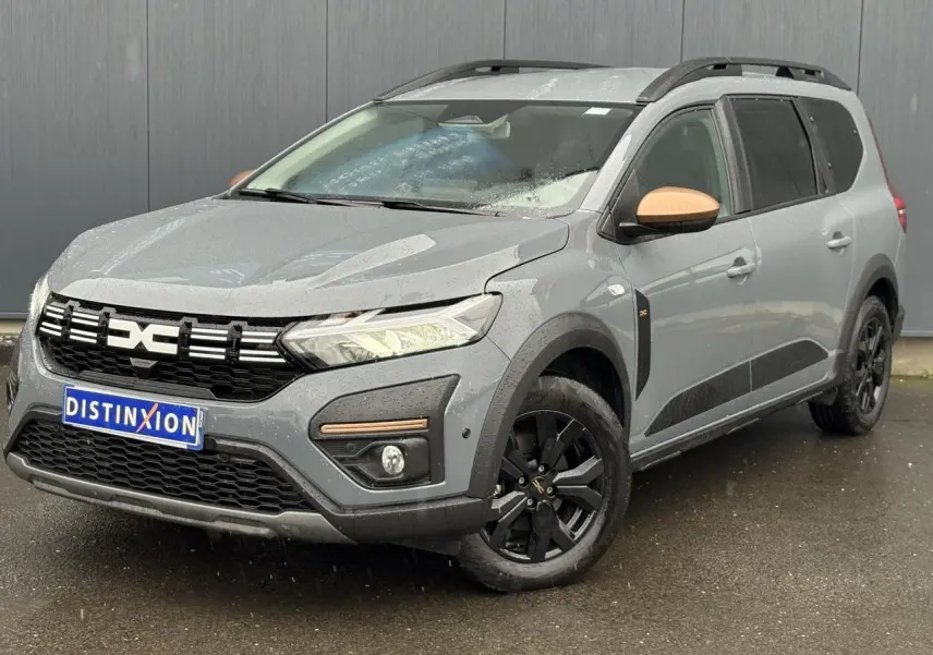 Vue 3/4 avant d'un Dacia Jogger gris urbain avec jantes noires et coques de rétroviseurs couleur cuivre.