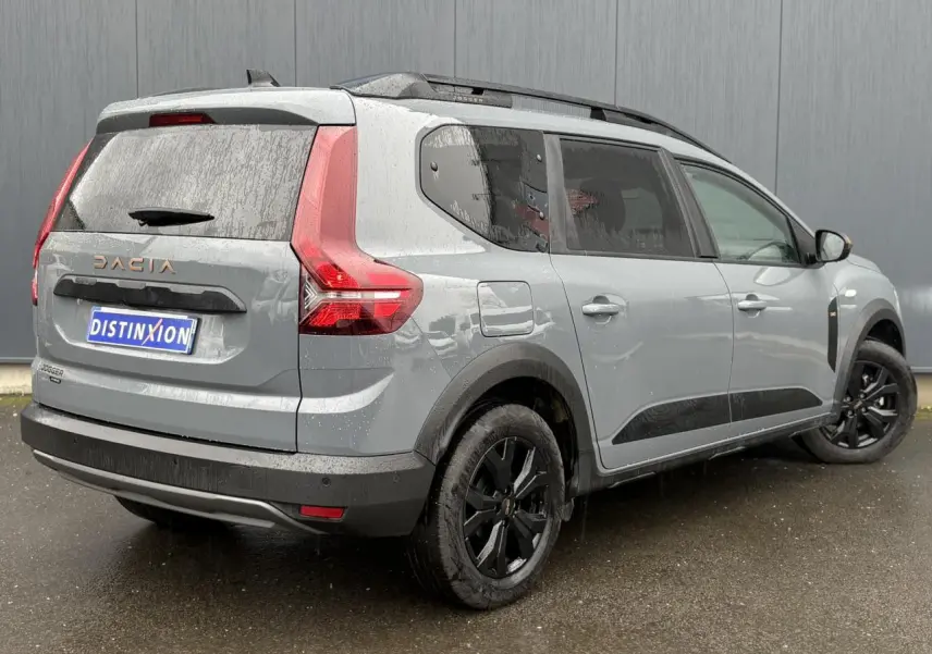 Vue 3/4 arrière droite du Dacia Jogger gris urbain 2025 avec jantes noires et barres de toit longitudinales.