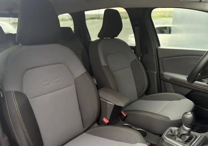Vue intérieure des sièges avant gris clair et foncé du Dacia Jogger 1.6 Hybrid 140 Extreme avec accoudoir central et levier de vitesse.