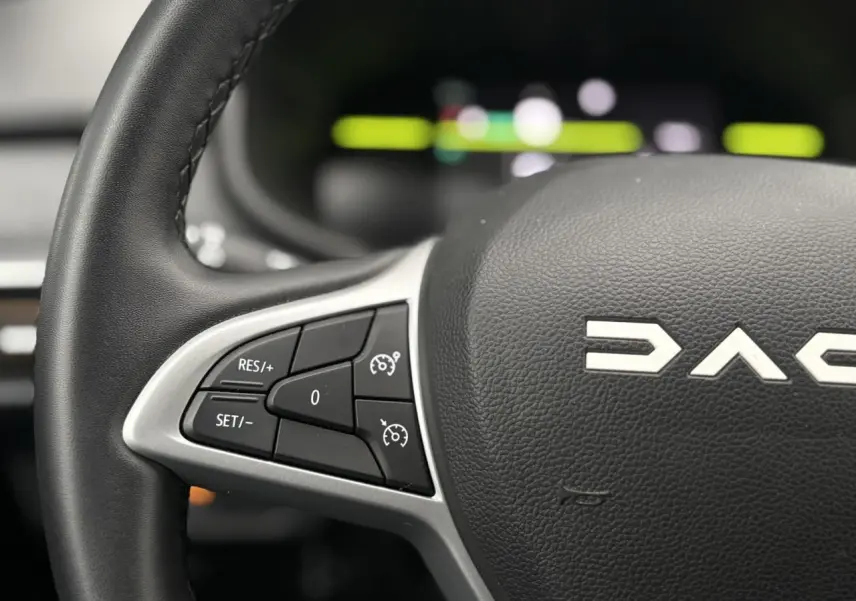 Gros plan sur le volant noir du Dacia Jogger gris urbain, avec commandes de régulateur de vitesse à gauche.