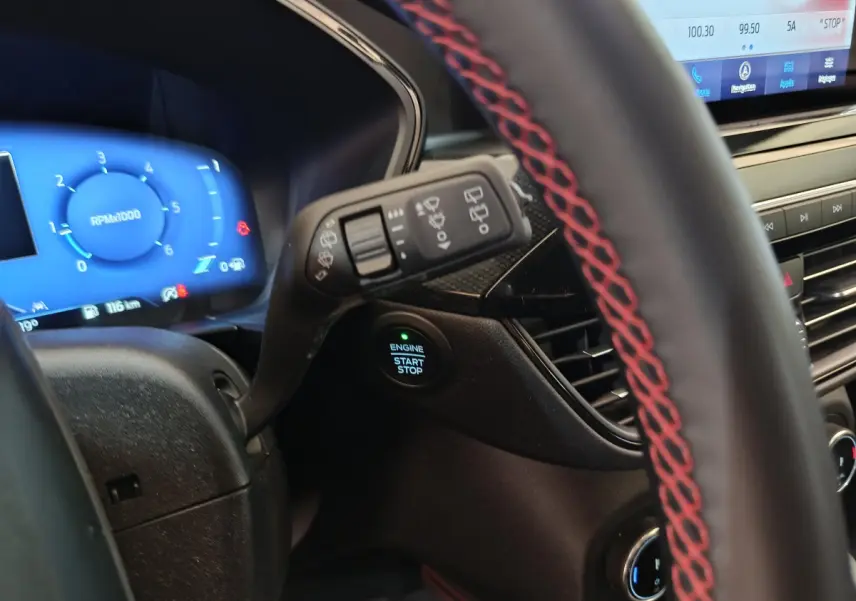 Gros plan intérieur sur le volant cuir noir avec surpiqûres rouges et tableau de bord digital bleu du Ford Kuga 2024.
