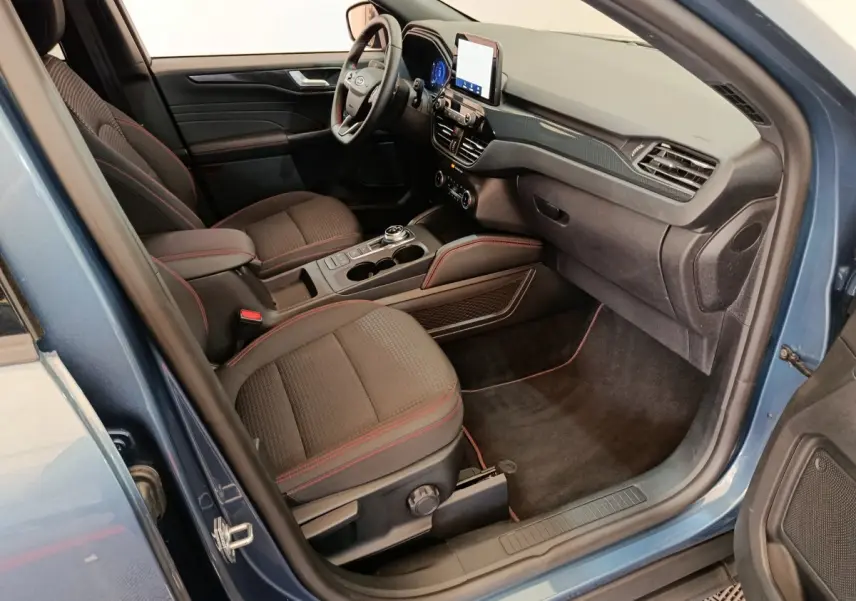 Intérieur avant droit du Ford Kuga bleu 2024, sièges noirs avec surpiqûres rouges et écran tactile central.
