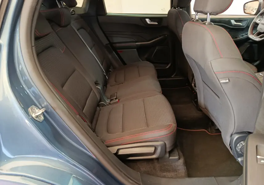 Vue intérieure côté gauche sur les sièges arrière noirs avec surpiqûres rouges du Ford Kuga bleu 2024 St Line.