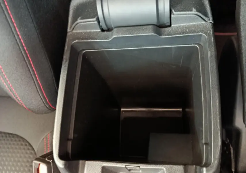 Vue plongeante sur le rangement central ouvert et siège noir avec surpiqûres rouges dans un Ford Kuga bleu 2024.