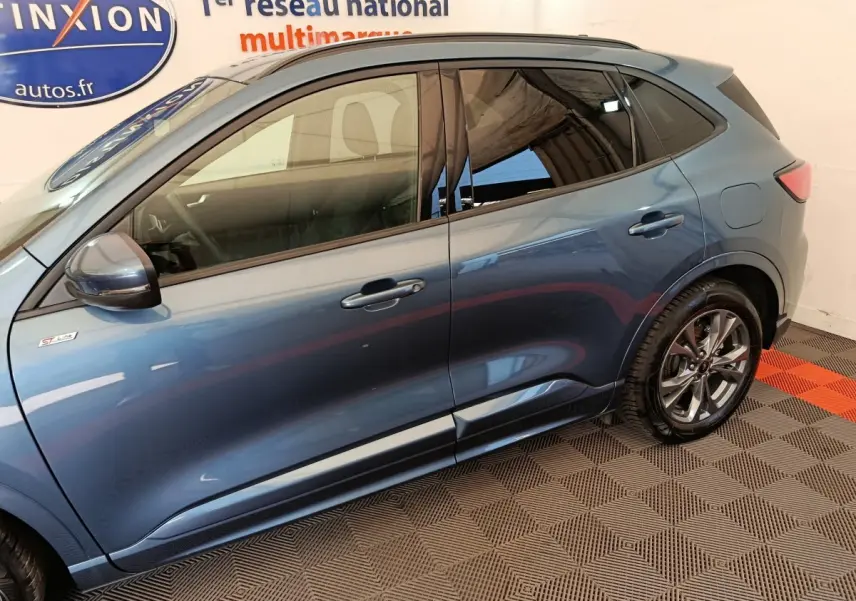 Vue latérale côté gauche d'un Ford Kuga bleu 2024 finition ST Line avec jantes alliage et rétroviseurs assortis.