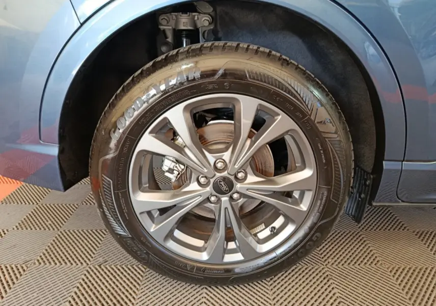 Gros plan sur la roue avant droite du Ford Kuga bleu 2024, avec jante alliage et pneu Goodyear visible.
