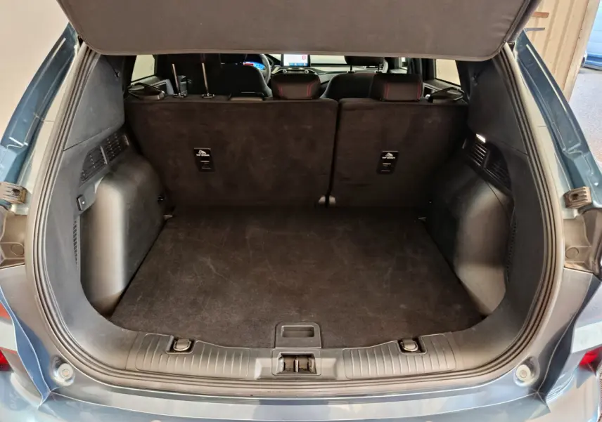 Vue arrière du coffre ouvert d'un Ford Kuga bleu 2024, montrant l'espace de chargement et la banquette arrière rabattue partiellement.