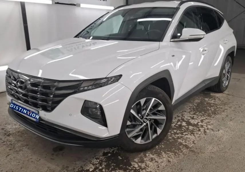 Hyundai Tucson blanc vu en 3/4 avant droit, avec calandre noire distinctive et jantes alliage modernes.