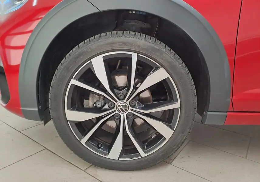 Gros plan sur la roue avant gauche d’un Volkswagen Taigo Rouge Roi avec jante alliage noir et argent brillante.