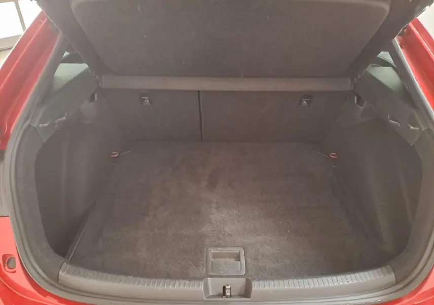 Coffre ouvert d’un Volkswagen Taigo Rouge Roi, vue plongeante sur l’espace de chargement vide et tapis noir.