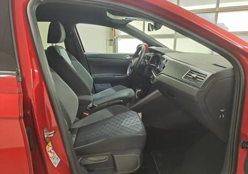 Vue intérieure côté conducteur du Volkswagen Taigo Rouge Roi 2021, sièges tissu noir avec motifs et tableau de bord moderne.