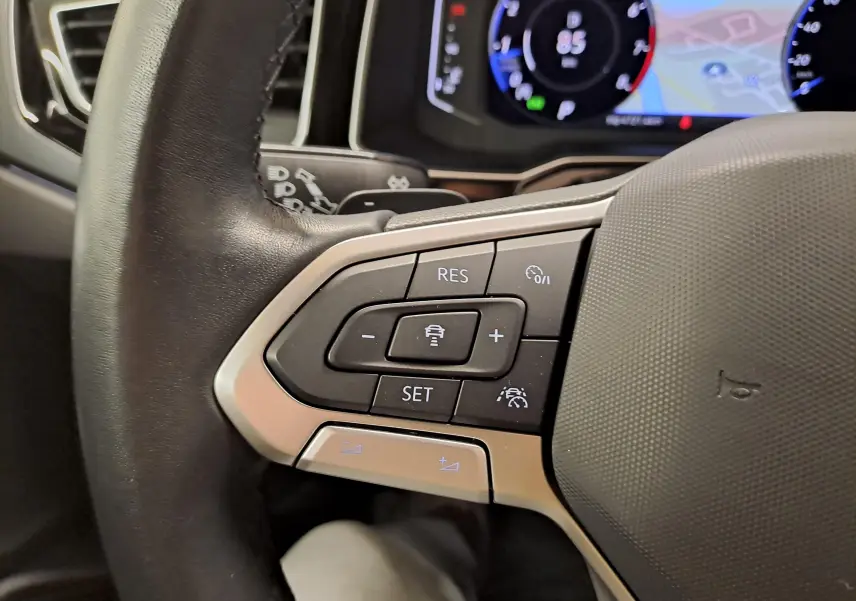 Gros plan sur les commandes au volant du Volkswagen Taigo 1.5 TSI 150 DSG7 R-LINE, avec affichage numérique en arrière-plan.