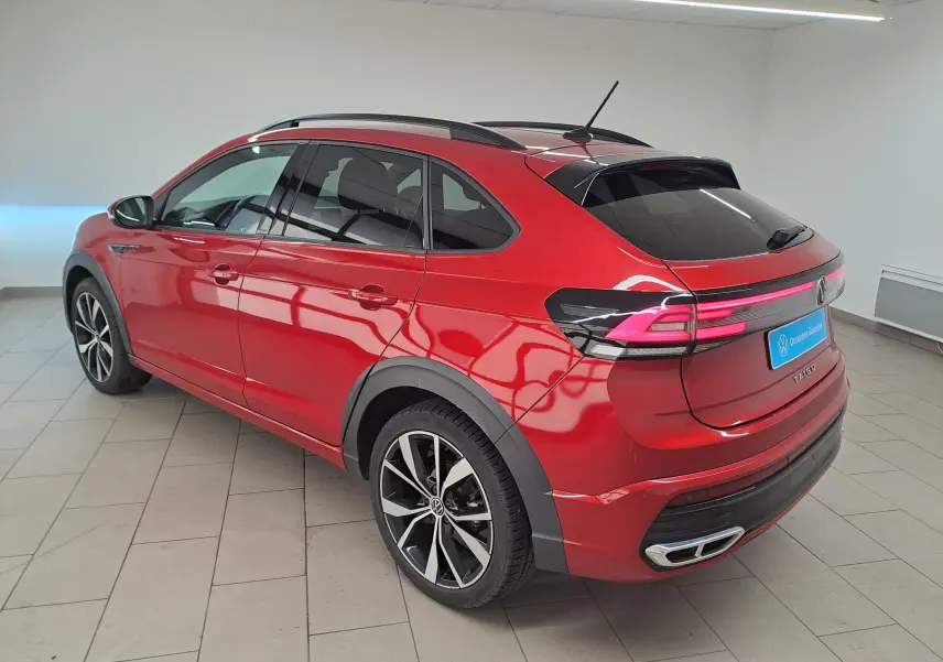 Vue 3/4 arrière droite du Volkswagen Taigo Rouge Roi, avec jantes noires brillantes et feux arrière LED allumés.