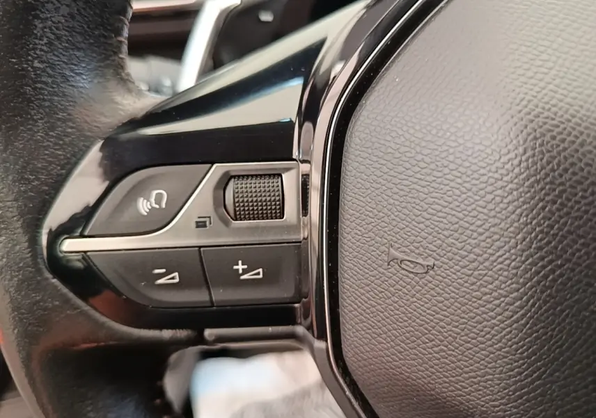 Gros plan sur le volant cuir noir multifonctions du Peugeot 3008 2022, avec commandes vocales et réglages de volume.