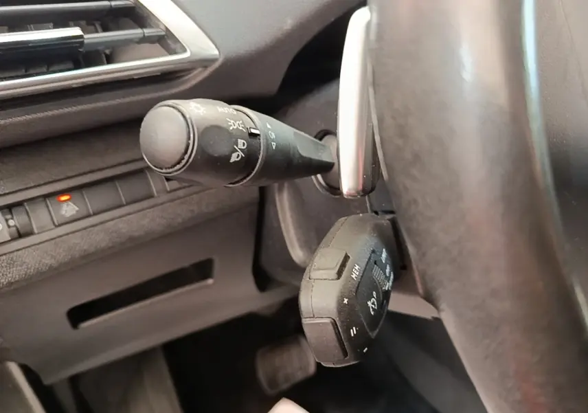 Gros plan sur la commande des feux et le volant cuir multi-fonctions du Peugeot 3008 gris foncé, côté gauche.