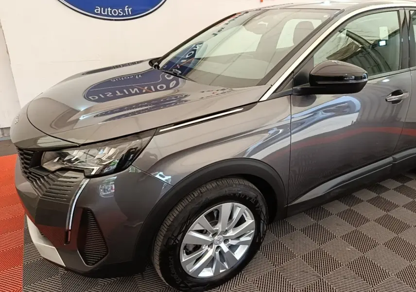 Vue 3/4 avant droit du Peugeot 3008 gris foncé avec phares LED et jantes alliage visibles en intérieur showroom.