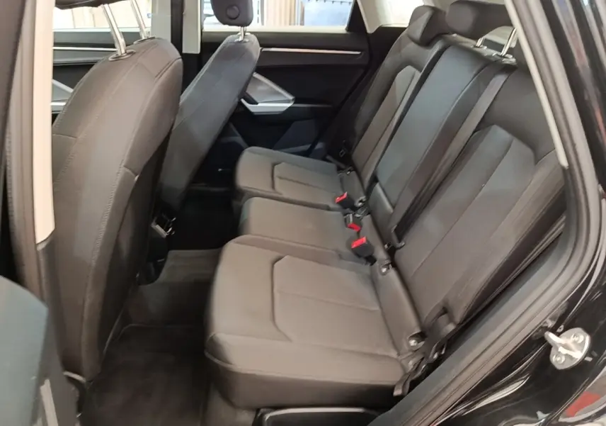 Vue latérale droite de l'habitacle arrière noir de l'Audi Q3 45 TFSI e 2023 avec sièges en tissu et ceintures de sécurité.