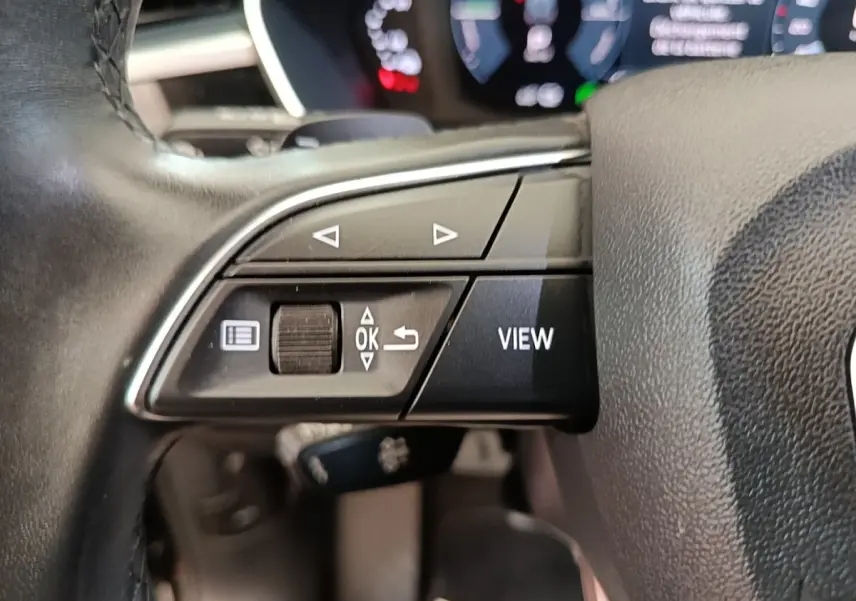 Gros plan sur le volant cuir noir multifonctions de l'Audi Q3 45 TFSI e avec commandes de navigation et bouton View.