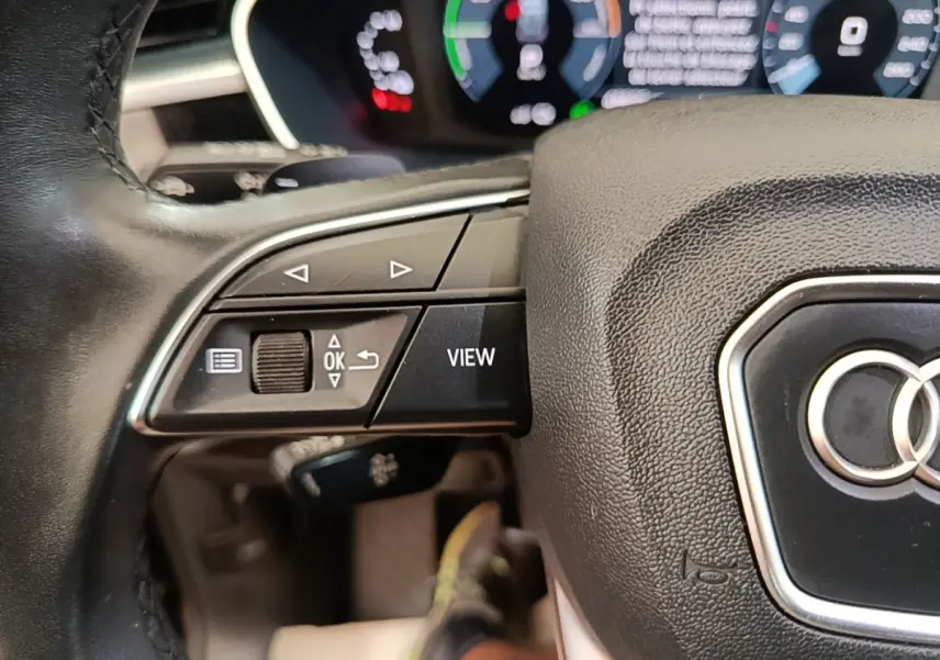 Gros plan sur le volant cuir multifonctions noir de l'Audi Q3 hybride rechargeable avec tableau de bord digital en arrière-plan.