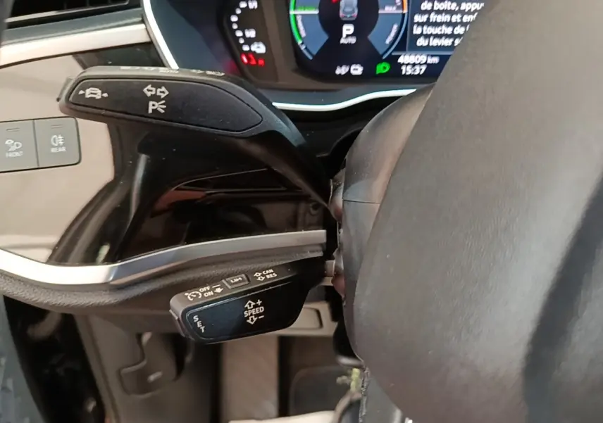 Gros plan sur les commandes au volant cuir noir de l'Audi Q3 hybride rechargeable, avec tableau de bord digital en arrière-plan.