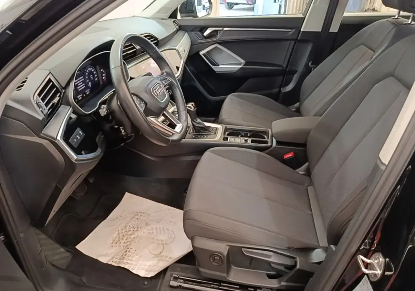 Intérieur avant droit de l'Audi Q3 45 TFSI e 2023 avec sièges gris, volant cuir multifonctions et tableau de bord digital.