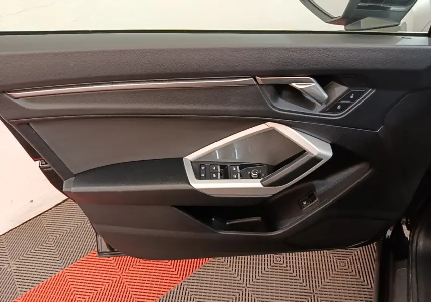 Vue intérieure côté gauche de la porte avant d'un Audi Q3 2023, avec commandes électriques et garniture noire.