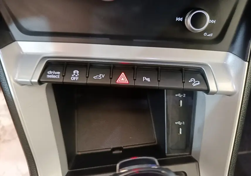 Gros plan sur la console centrale grise de l'Audi Q3 45 TFSI E avec boutons de contrôle et ports USB visibles.
