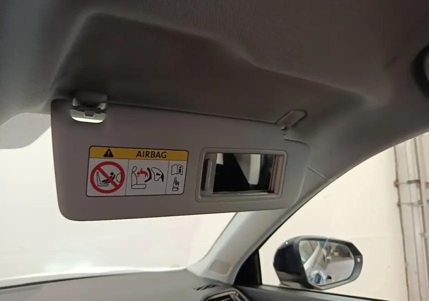 Détail intérieur du pare-soleil côté conducteur avec miroir et avertissement airbag, rétroviseur extérieur visible.