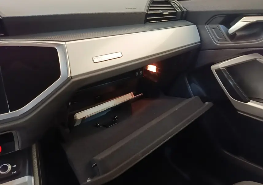 Intérieur Audi Q3 2023 vue côté passager, boîte à gants ouverte avec éclairage et tableau de bord gris clair.