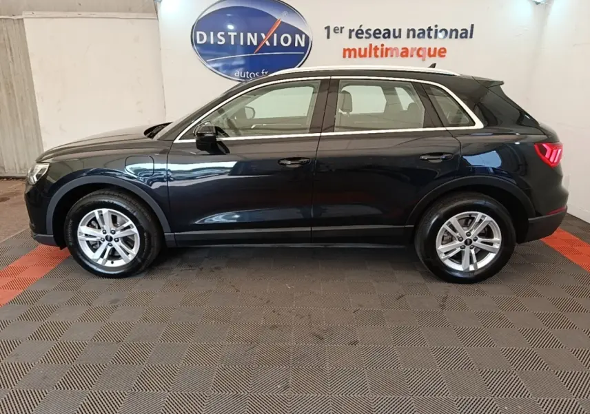 Vue de profil côté gauche d’un Audi Q3 hybride rechargeable 2023 noir avec jantes argentées en intérieur showroom.