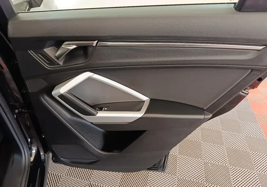 Vue rapprochée de la porte intérieure arrière gauche noire avec poignée argentée et commandes de vitre Audi Q3 2023.