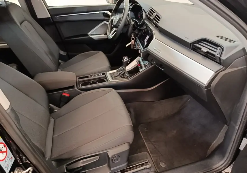 Intérieur avant droit de l'Audi Q3 45 TFSI e 2023 avec sièges gris, volant cuir multifonctions et tableau de bord moderne.