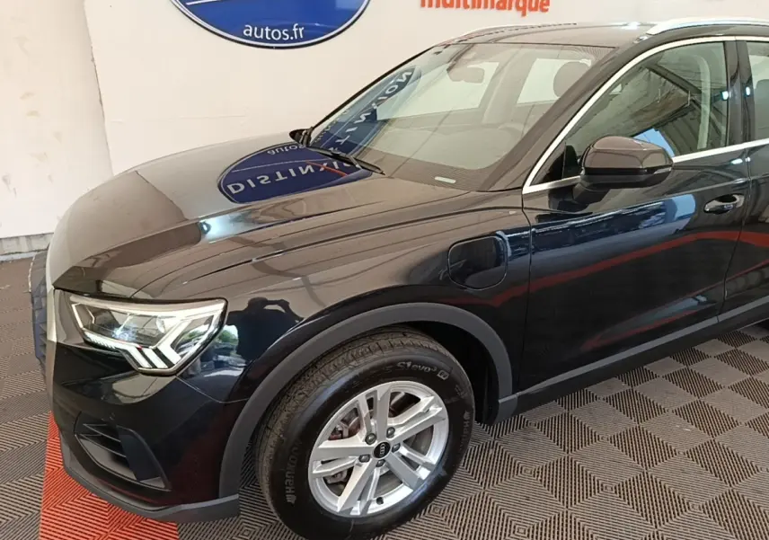 Vue 3/4 avant droit d’un Audi Q3 hybride rechargeable noir avec jantes alliage et prises de recharge visibles sur l’aile avant.