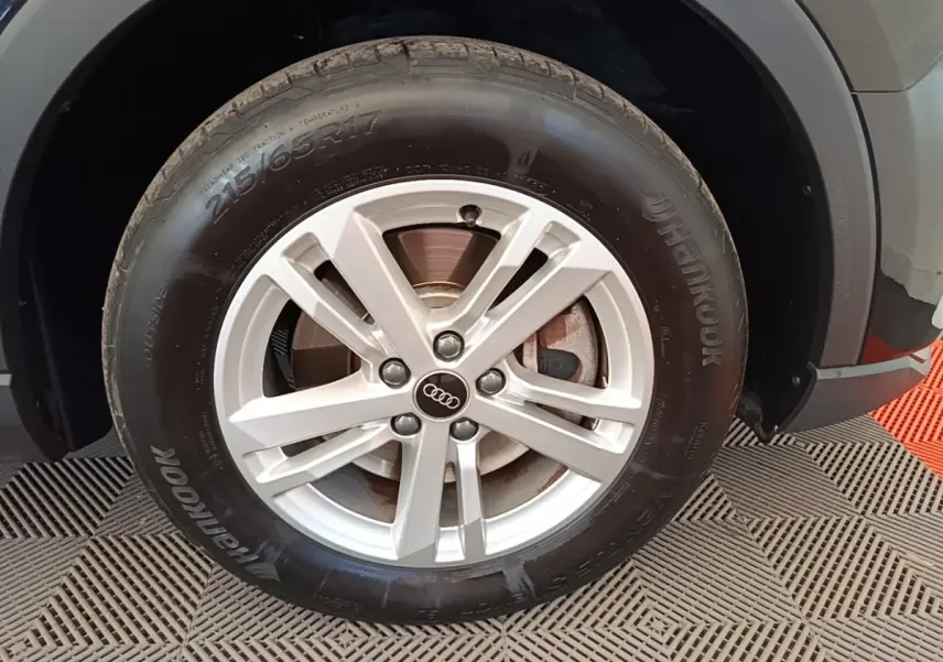 Gros plan sur la roue avant droite d'un Audi Q3 45 TFSI E 245 gris avec jante alliage et logo Audi central.