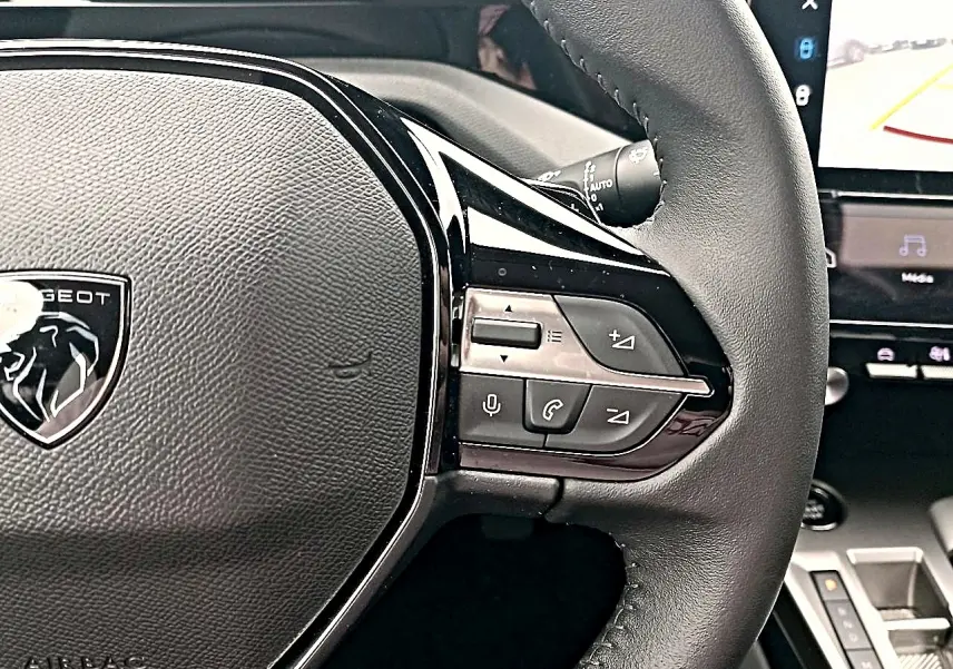 Gros plan sur le volant cuir noir de la Peugeot 408 Hybrid 145 allure, avec commandes multifonctions et logo lion central.