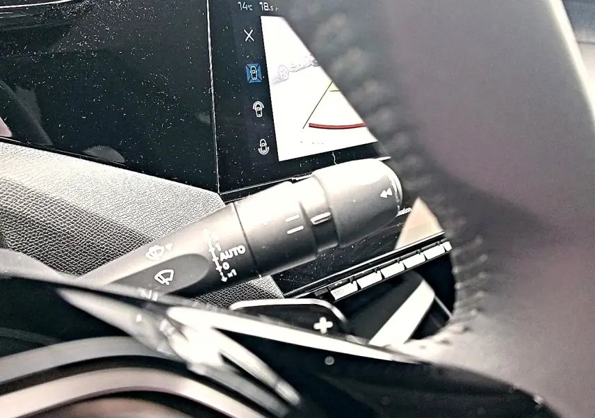 Gros plan sur la commande d’essuie-glace et l’écran tactile du tableau de bord d’une Peugeot 408 Hybrid 145 gris sélénite.