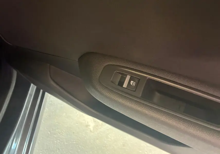 Gros plan sur le bouton de commande de la vitre électrique côté gauche dans une Renault Clio gris foncé, version 2020.