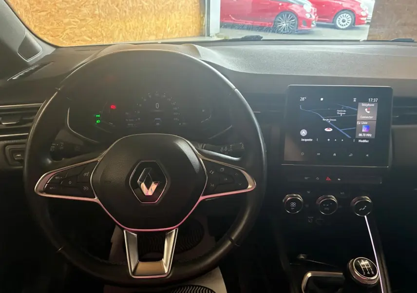 Vue intérieure centrée sur le volant Renault d'une Clio gris, avec tableau de bord numérique et écran tactile GPS.