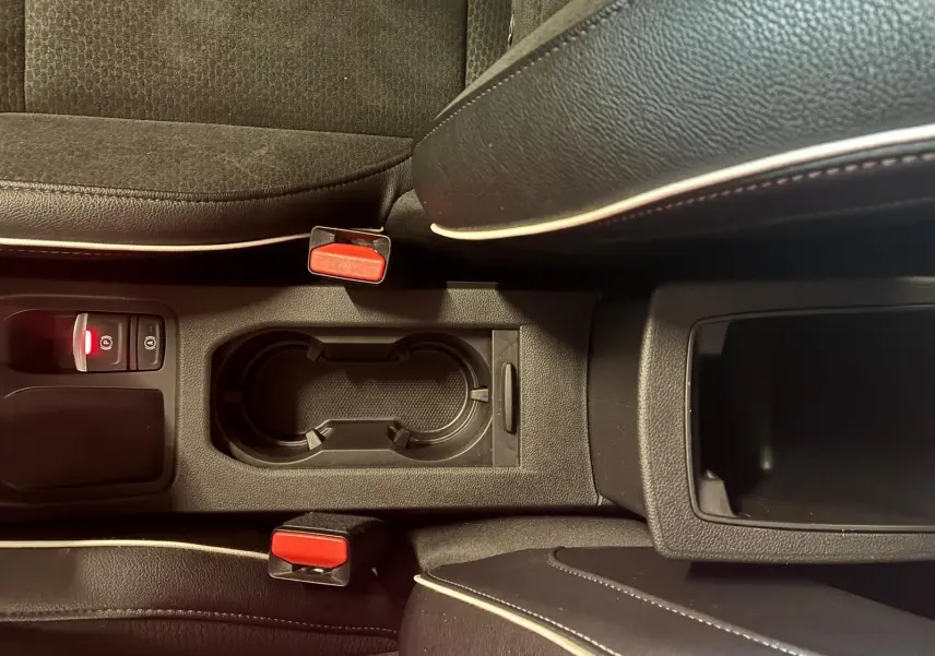 Vue rapprochée de la console centrale de la Renault Clio 2020 gris, avec porte-gobelets et ceintures rouges visibles.