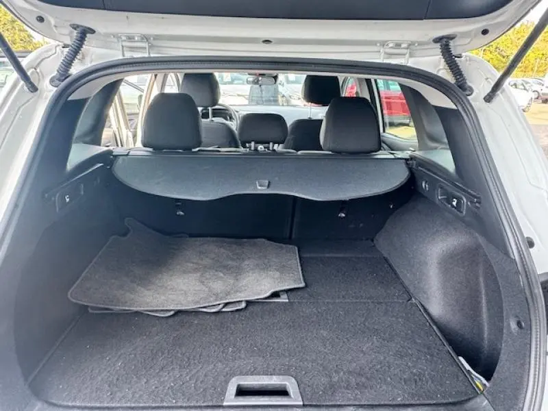 Coffre ouvert vu de l'arrière d'un Renault Kadjar blanc, avec tapis de sol gris et banquette arrière noire visible.
